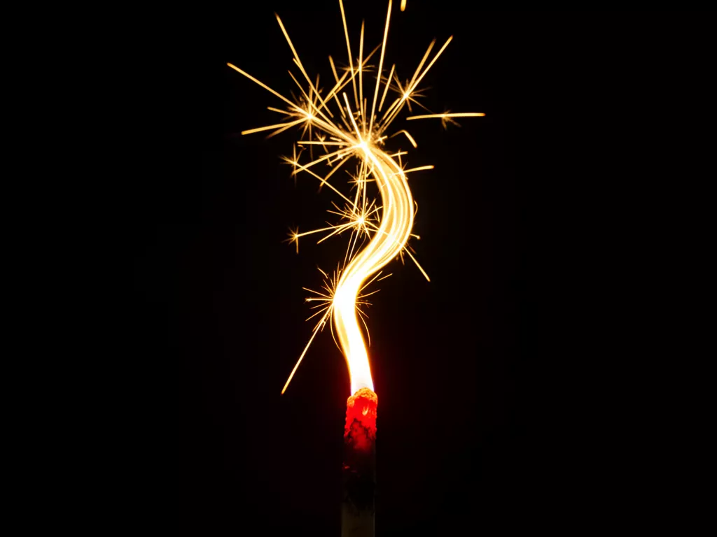 A minimalist macro photo of a single golden spark bursting upward from a glowing red ember